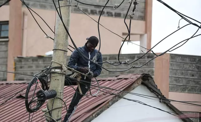 FILE -A man connects electric cables on a pole above the Kibera informal settlement in Nairobi, Kenya, March 31, 2026. (AP Photo/Henry Naminde, File)