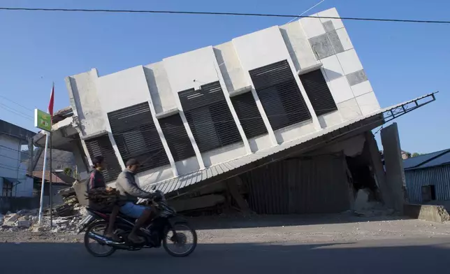 Motorists ride past a building that collapsed during an earthquake in Reo, East Nusa Tenggara province, Indonesia, Monday, Aug. 17, 2026. (AP Photo/Firdia Lisnawati)