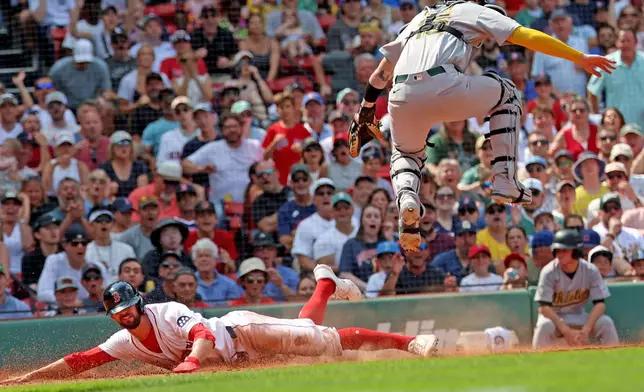 Boston Red Sox's Eli White, left, slides to home plate to score as Athletics catcher Jonah Heim, top right, leaps out of the way during the fifth inning of a baseball game, Sunday, Aug. 9, 2026, in Boston. (AP Photo/Mark Stockwell)