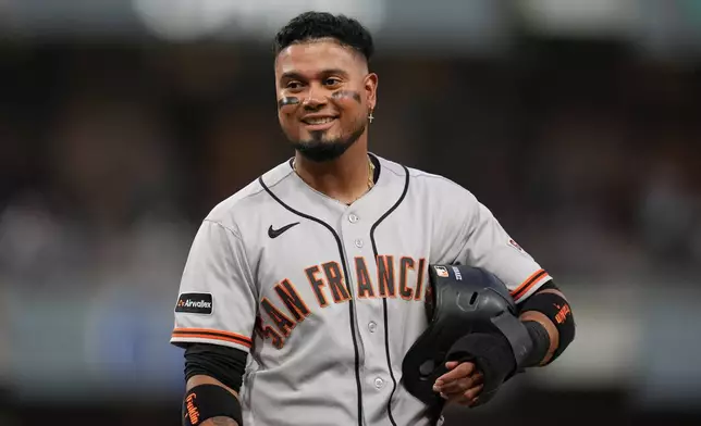 San Francisco Giants' Luis Arraez jokes with players in the San Diego Padres dugout as he stands on first base after getting hit by a pitch during the fourth inning of a baseball game Thursday, July 30, 2026, in San Diego. (AP Photo/Gregory Bull)