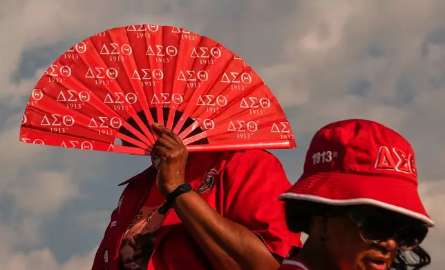 A demonstrator shields herself from the sun with a fan before the March on Washington, Friday, Aug. 28, 2026, near the Lincoln Memorial in Washington. (AP Photo/Julia Demaree Nikhinson)