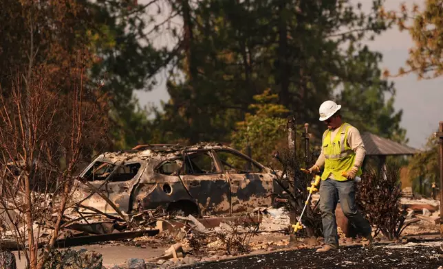 A worker with Avista moves through a property after a wildfire hit the northern part of Spokane, Wash., Monday, Aug. 3, 2026. (AP Photo/Lindsey Wasson)