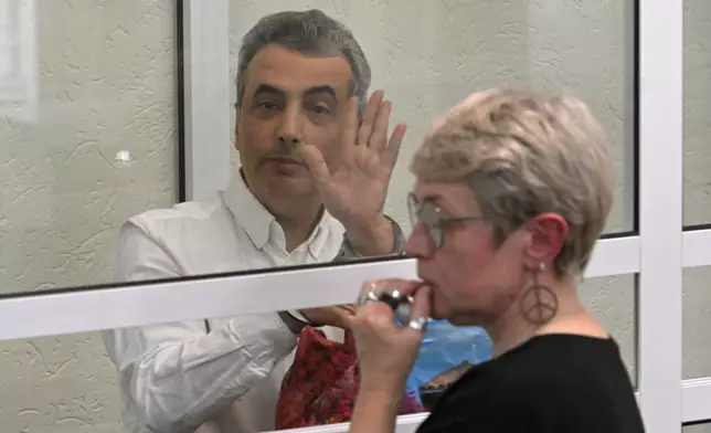Lev Shlosberg, left, senior member of the Yabloko party, waves standing in the defendant's box after a verdict in the case against him is delivered, in a court in Pskov, Russia, Monday, Aug. 17, 2026, with his wife Zhanna Shlosberg on the right. (AP Photo)