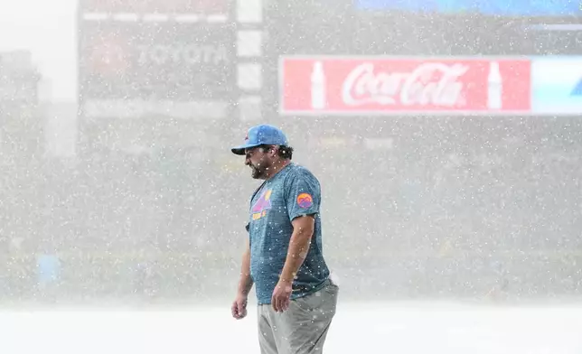 A member of the Coors Field grounds crew stands on the tarpaulin as a storm packing heavy rain and hail sweeps over the stadium before the Colorado Rockies host the Kansas City Royals in a baseball game Friday, July 31, 2026, in Denver. (AP Photo/David Zalubowski)