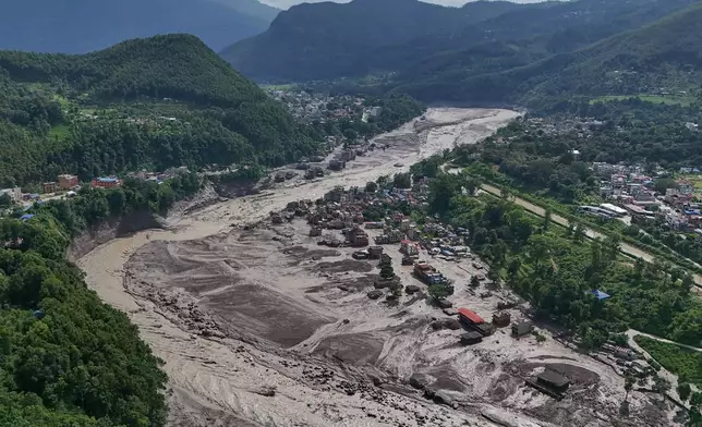 Damaged houses stand precariously near the swollen, debris-choked banks of the Trishuli River after flash floods in Nepal's Nuwakot district on Wednesday, Aug. 26, 2026. (AP Photo/Niranjan Shrestha)