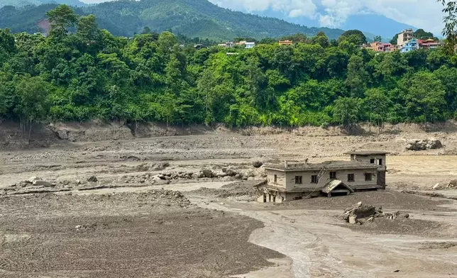 A damaged house stands precariously near the swollen, debris-choked banks of the Trishuli River after a flash floods in Nepal's Nuwakot district on Wednesday, Aug. 26, 2026. (AP Photo/Niranjan Shrestha)