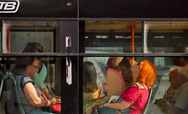 A woman uses a fan to cool off while riding a bus on a hot day, as the National Weather forecaster issued an extreme heat code red warning for most parts of the country, in Bucharest, Romania, Thursday, Aug. 6, 2026. (AP Photo/Vadim Ghirda)