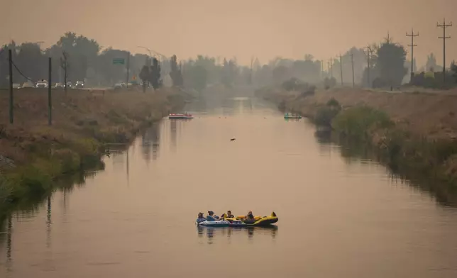 People float on the Channel Pathway that connects Okanagan Lake and Skaha Lake as smoke from wildfires burning in the region fills the air, in Penticton, British Columbia, Monday, Aug. 10, 2026. (Darryl Dyck/The Canadian Press via AP)
