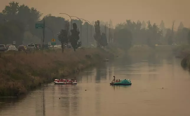 People float on the Channel Pathway that connects Okanagan Lake and Skaha Lake as smoke from wildfires burning in the region fills the air, in Penticton, British Columbia, Monday, Aug. 10, 2026. (Darryl Dyck/The Canadian Press via AP)