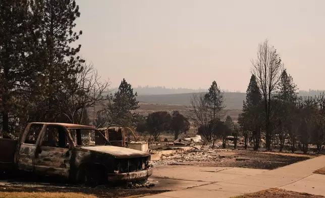 A burned truck sits in a driveway near several destroyed homes in a residential neighborhood Tuesday, Aug. 4, 2026, after a wildfire hit the northern part of Spokane, Wash. (AP Photo/Lindsey Wasson)