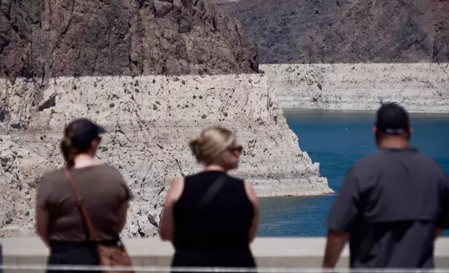 Tourists on the Hoover Dam look out at the bathtub ring of minerals that shows the former water levels of Lake Mead near Boulder City, Nev., on Friday, Aug. 7, 2026. (AP Photo/Ty ONeil)