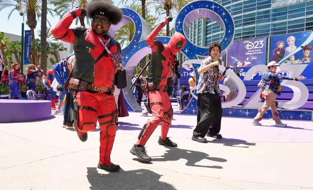 Mohamed Obsidye, left, of Columbus, Ohio, dressed as his own superhero character "Afro-Pool," leads a dance outside the entrance to D23: The Ultimate Disney Fan Event on Friday, Aug. 14, 2026, at the Anaheim Convention Center in Anaheim, Calif. (AP Photo/Chris Pizzello)