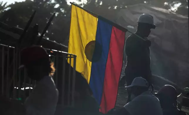 A firefighter working on rescue efforts holds a Colombian flag amid the rubble three days after an earthquake struck Cali, Colombia, Thursday, Aug. 13, 2026. (AP Photo/Ivan Valencia)