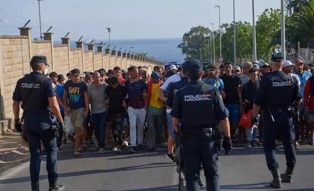 Migrants who crossed from Morocco into Spain are escorted by Spanish police to temporary shelters after being cleared from a beach in the Spanish exlave of Ceuta on Thursday, Aug. 20, 2026. (AP Photo/Antonio Sempere)