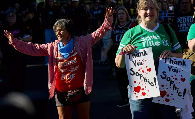 A counter protestor, left, raises her arms next to people rallying to support Indiana Fever guard Sophie Cunningham after her comments on transgender athletes in women's sports before a WNBA basketball game between the Portland Fire and the Indiana Fever in Portland, Ore., Friday, July 31, 2026. (AP Photo/Craig Mitchelldyer)