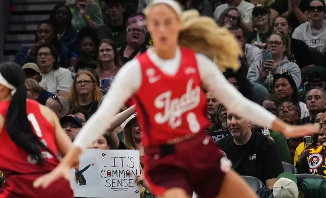 Indiana Fever guard Sophie Cunningham, front, runs by a fan holding a sign referencing her comments on transgender athletes and women's sports during the first half of a WNBA basketball game against the Seattle Storm, Tuesday, July 28, 2026, in Seattle. (AP Photo/Lindsey Wasson)