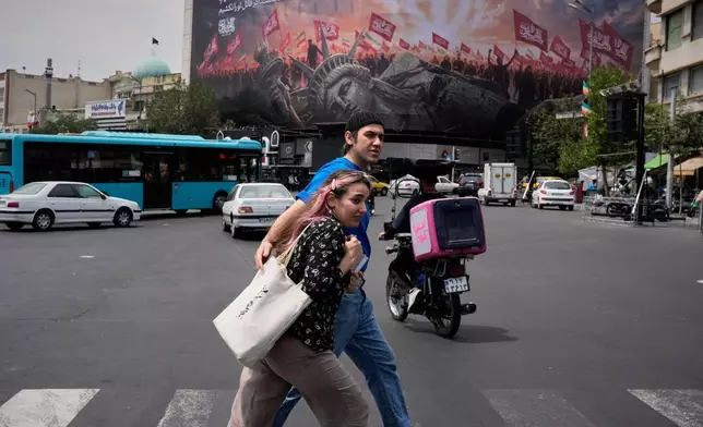 Pedestrians cross a street in front of a billboard depicting a fallen Statue of Liberty and crowds carrying Iranian and Shiite flags at Revolution Square in Tehran, Iran, Monday, Aug. 3, 2026. (AP Photo/Vahid Salemi)