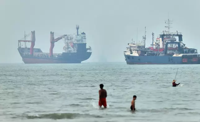 FILE - Children wade in the water with cargo ships at anchor in the background and a fisherman nearby, in the Strait of Hormuz off Bandar Abbas, Iran, Tuesday, June 30, 2026. (Amirhosein Khorgooi/ISNA via AP,File)
