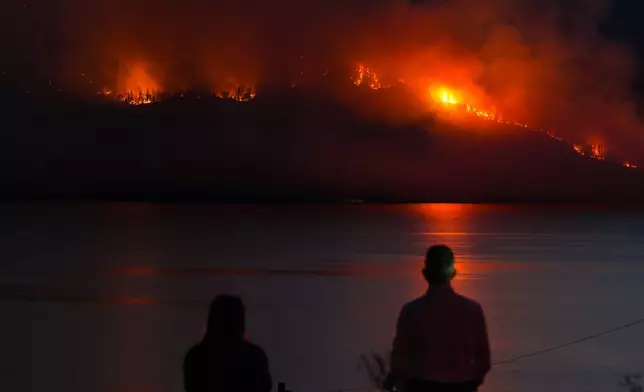 FILE - People in Lake Country, British Columbia, watch as the Quilpituk Creek wildfire burns on the mountainside across Okanagan Lake, near Fintry, Aug. 3, 2026. (Darryl Dyck/The Canadian Press via AP, File)