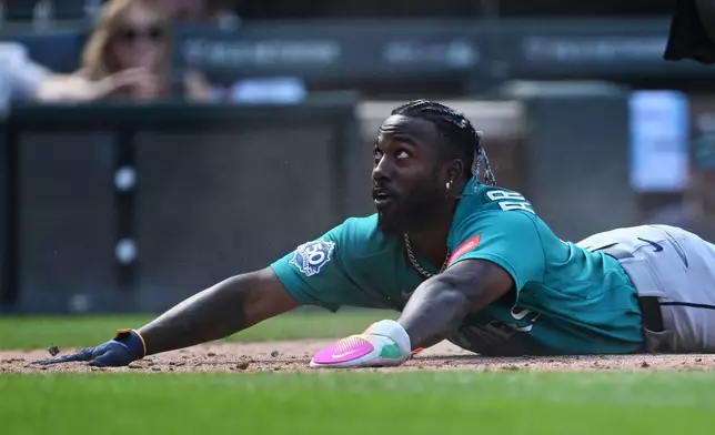 Seattle Mariners' Randy Arozarena looks up at a teammate after sliding safely into home in the fourth inning against the Colorado Rockies during a baseball game Sunday, Sept. 20, 2026, in Denver. (AP Photo/RJ Sangosti)