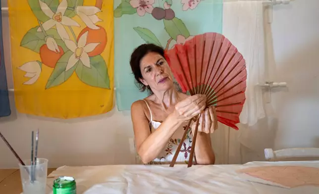 Silvia Ramos López, owner of Manos de Agua, glues red silk to the sticks of a handmade fan at her workshop in Seville, Spain, on Aug. 25, 2026. (AP Photo/Laura Leon)