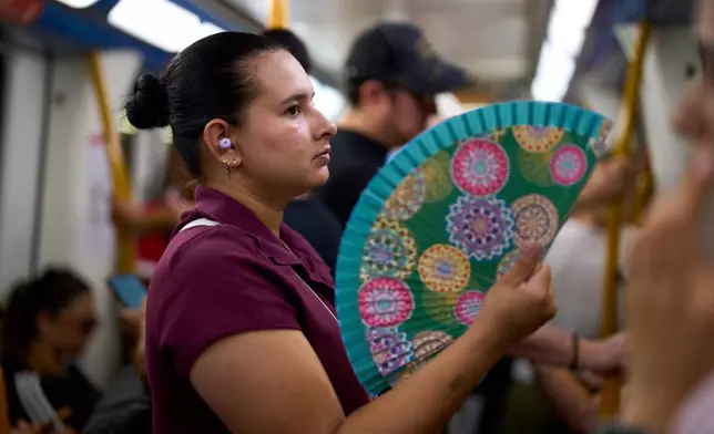 A woman uses a fan to cool herself on the subway in Madrid, Spain, on Aug. 18, 2026. (AP Photo/Manu Fernandez)