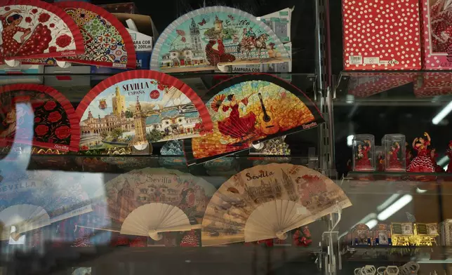 Mass-produced fans featuring tourist images of Seville are displayed in a shop window in Seville, Spain, on Aug. 25, 2026. (AP Photo/Laura Leon)