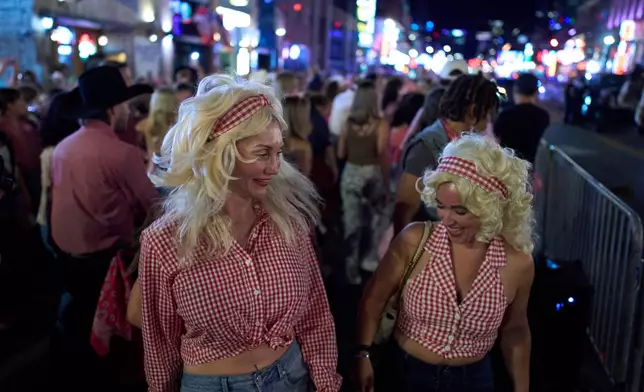 Danielle Maples, left, and Heather Lucas, right, dressed in Dolly Parton costumes dance with a flash mob on Broadway Friday, Sept. 25, 2026, in Nashville, Tenn. during a Dolly Parton Day event honoring the late country music artist. (AP Photo/George Walker IV)