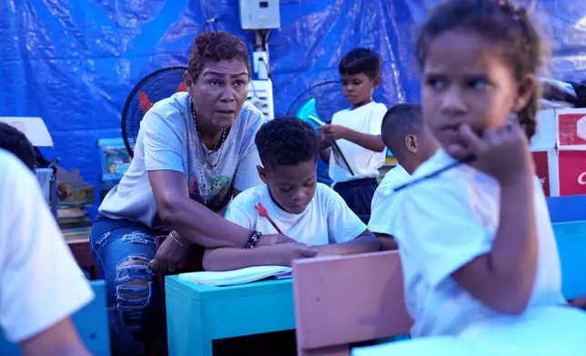 Teacher Jazmín Urimare gives a math class under a tent at a improvised school inside the camp where they all live since being displaced by the earthquake in La Guaira, Venezuela, Monday, Sept. 14, 2026. (AP Photo/Ariana Cubillos)