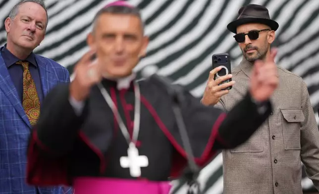 French artist Jean René, known as JR, right, and American letterpress artist Bill Moran, left, listen to Bishop Giacomo Cardinali, vice prefect of the Vatican Library, at the Vatican, Monday, Sept. 14, 2026, during a press preview of the exhibit "AQVA, Catastrophe and Wonder," which will be open to the public from Sept. 25 through May 14, 2027. (AP Photo/Andrew Medichini)