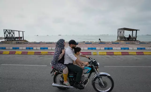 A man, woman and boy ride a motorcycle along the waterfront as commercial vessels lie anchored in the Strait of Hormuz off Bandar Abbas, Iran, Friday, Sept. 4, 2026. (AP Photo/Vahid Salemi)