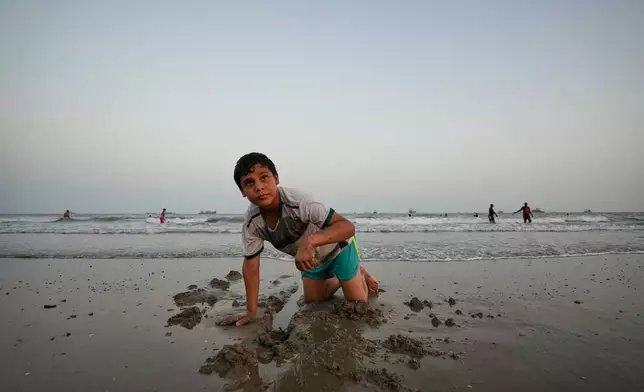 A boy plays in wet sand as others swim and commercial vessels lie anchored in the Strait of Hormuz off Bandar Abbas, Iran, Friday, Sept. 4, 2026. (AP Photo/Vahid Salemi)