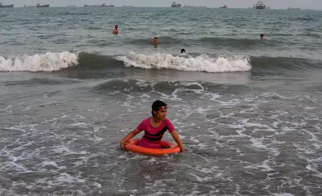 A girl plays in the water with a swim ring as commercial vessels lie anchored in the Strait of Hormuz off Bandar Abbas, Iran, Friday, Sept. 4, 2026. (AP Photo/Vahid Salemi)