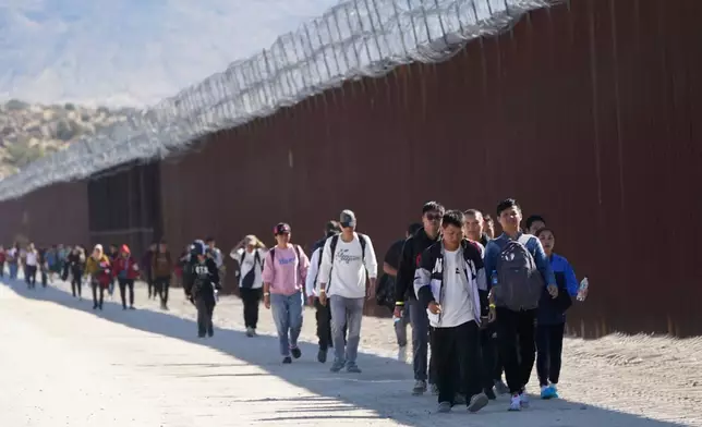 FILE - A group of people, including many from China, walk along the wall after crossing the border with Mexico to seek asylum, Oct. 24, 2023, near Jacumba, Calif. (AP Photo/Gregory Bull, File)