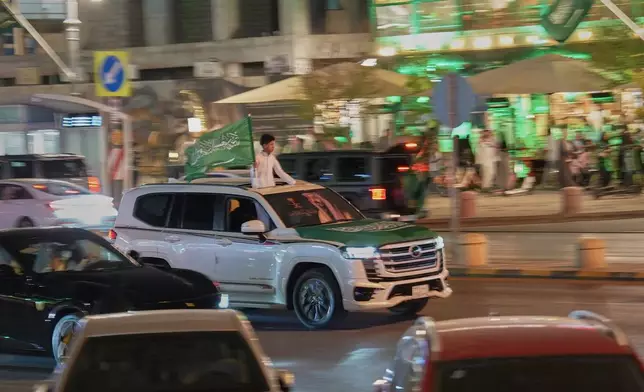 A young man holds a Saudi flag while standing through the sunroof of a vehicle during celebrations marking Saudi Arabia's 96th National Day in Riyadh, Saudi Arabia, Wednesday, Sept. 23, 2026. (AP Photo/Baraa Anwer)