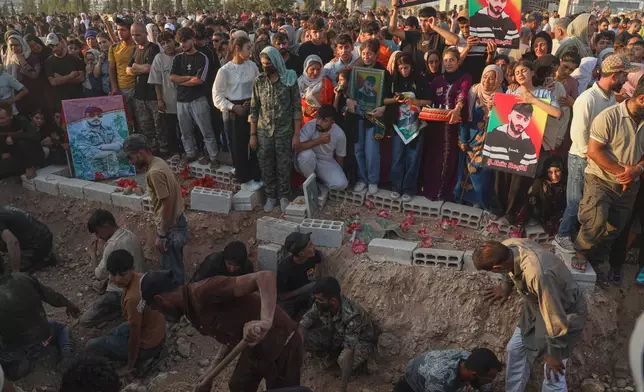 Mourners holding portraits gather beside graves during a mass funeral for prisoners who died in a fire that broke out during unrest at the local prison in the predominantly Kurdish city of Kobani, northern Syria, Monday, Sept. 14, 2026. (AP Photo/Baderkhan Ahmad)