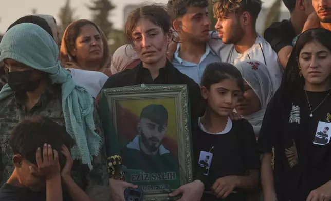 A mourner holds a portrait of one of the prisoners who died in a fire that broke out during unrest at the local prison, during a mass funeral in the predominantly Kurdish city of Kobani, northern Syria, Monday, Sept. 14, 2026. (AP Photo/Baderkhan Ahmad)
