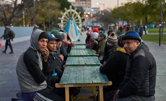 Men wait to receive free food after attending a Mass organized by the Catholic Church at a square outside the Constitución train station in Buenos Aires, Argentina, Tuesday, Sept. 22, 2026. (AP Photo/Rodrigo Abd)
