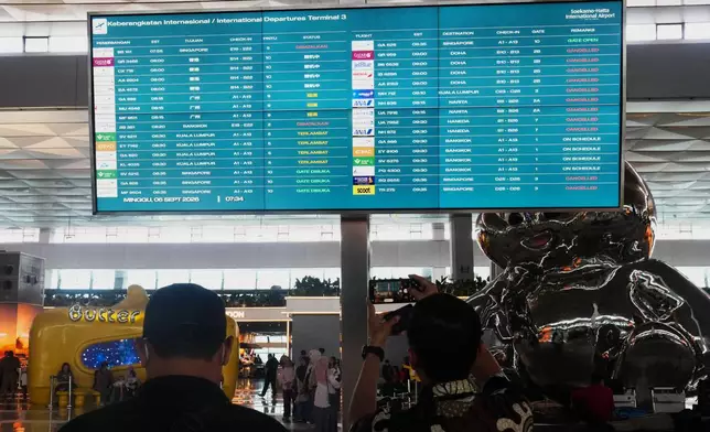 Travelers walk past an information board showing disrupted flights at Soekarno-Hatta International Airport in Tangerang, Indonesia, Sunday, Sept. 6, 2026. (AP Photo/Tatan Syuflana)