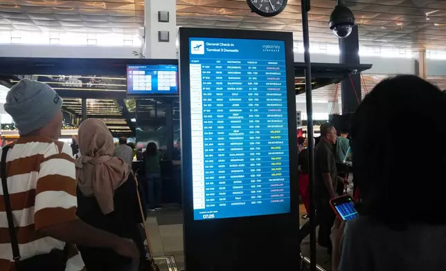 Travelers walk past an information board showing disrupted flights at Soekarno-Hatta International Airport in Tangerang, Indonesia, Sunday, Sept. 6, 2026. (AP Photo/Tatan Syuflana)