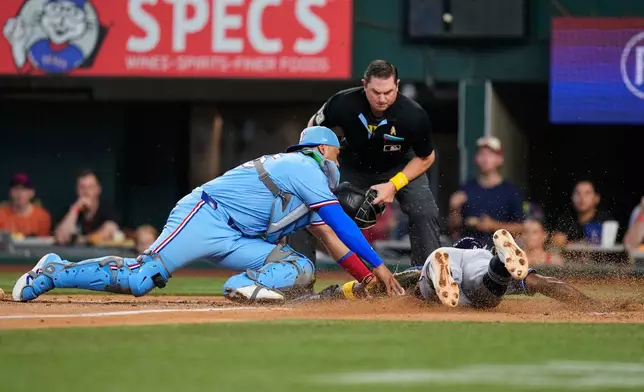 Texas Rangers catcher Elias Díaz is unable to get a tag on Tampa Bay Rays' Jorge Mateo, right, who scored on a sacrifice bunt by Nick Fortes as umpire Derek Thomas, rear, looks on in the second inning of a baseball game Sunday, Sept. 6, 2026, in Arlington, Texas. (AP Photo/Tony Gutierrez)
