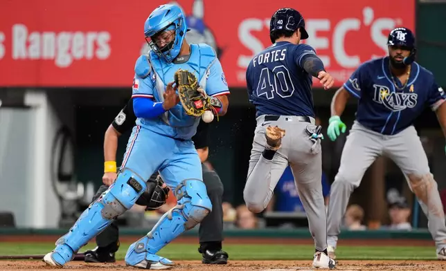 Texas Rangers catcher Elias Díaz bobbles the throw to the bag as Tampa Bay Rays' Nick Fortes (40) scores on a Jonathan Aranda sacrifice fly during the second inning of a baseball game Sunday, Sept. 6, 2026, in Arlington, Texas. (AP Photo/Tony Gutierrez)