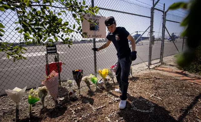 A person adjusts flowers at a memorial for Eliana Moreno and George Marciniw who died in a helicopter crash at the site where their helicopter used to park at Whiteman Airport in Los Angeles, Wednesday, Sept. 16, 2026. (AP Photo/Ethan Swope)