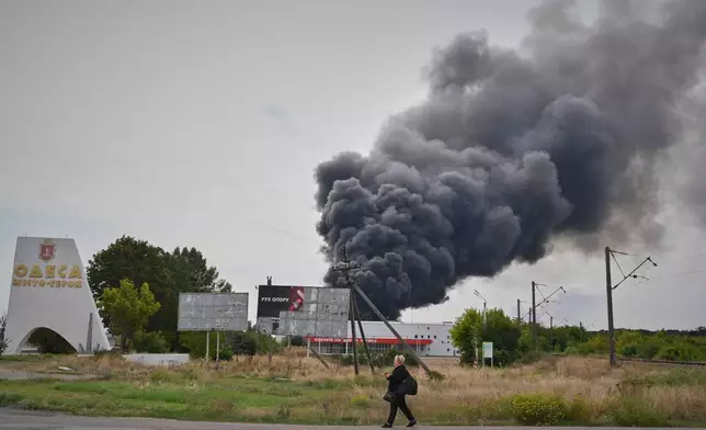 A woman walks by the burning warehouse at the city entrance following Russian air attack in Odesa, Ukraine, Sunday, Sept. 13, 2026. (AP Photo/Michael Shtekel)