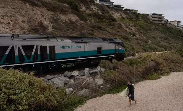 A surfer walks along North Beach as a Metrolink train travels along the coast in San Clemente, Calif., Friday, Sept. 18, 2026. (AP Photo/Jae C. Hong)