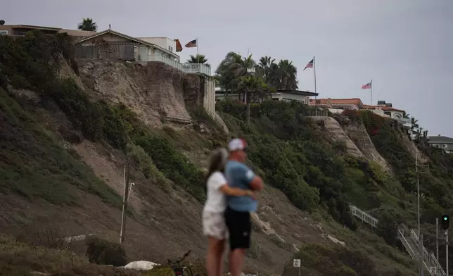 A couple hug at North Beach as crumbling seaside bluffs are seen behind them in San Clemente, Calif., Friday, Sept. 18, 2026. (AP Photo/Jae C. Hong)