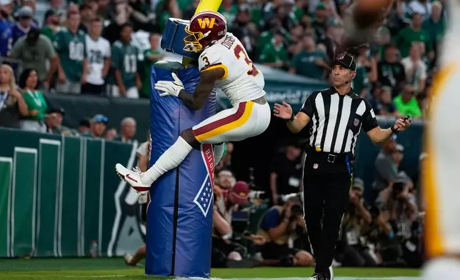 Washington Commanders wide receiver Stefon Diggs (3) jumps on the goal post as he celebrates his touchdown against the Philadelphia Eagles during the second half of an NFL football game, Sunday, Sept. 13, 2026, in Philadelphia. (AP Photo/Matt Slocum)