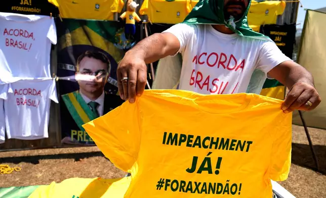 A vendor holds up a T-shirt that reads in Portuguese: "Impeachment now! Out with Xandao," a nickname for Supreme Court Justice Alexandre de Moraes, during a protest by supporters of presidential candidate Sen. Flavio Bolsonaro calling for Moraes' impwldeachment in Brasilia, Brazil, Tuesday, Sept. 15, 2026. (AP Photo/Eraldo Peres)