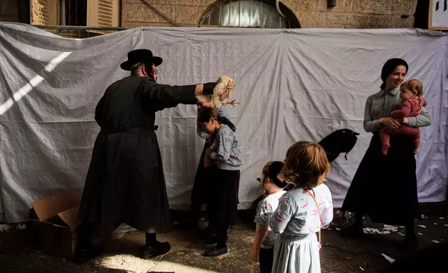 An ultra-Orthodox Jewish man swings a chicken over his children's heads as part of the Kaparot ritual ahead of the Jewish holiday of Yom Kippur in Jerusalem, Thursday, Sept. 17, 2026. (AP Photo/Ohad Zwigenberg)
