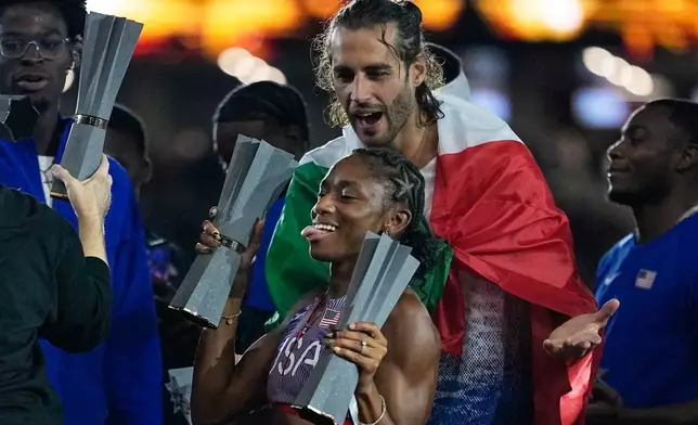 High jumper Gianmarco Tamberi, of Italy, looks at Melissa Jefferson-Wooden, of the United States, holding her two trophies for the women's 100 and 200 meters at the end of the World Athletics Ultimate Championship in Budapest, Hungary, Sunday, Sept. 13, 2026. (AP Photo/Matthias Schrader)